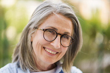 An older woman wearing glasses smiles directly at the camera.