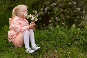 Little girl in pink dress in the garden. Girl sitting with blooming branch and snuffles their. Spring day