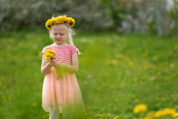 Little girl Thoughtful on meadow with dandelions. Fair-haired girl wears wreath of flowers. Summer vacation time.