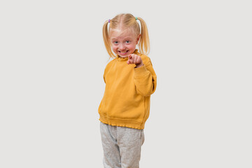 Portrait of a cute little girl in a yellow hoodie and gray pants pointing at the camera.