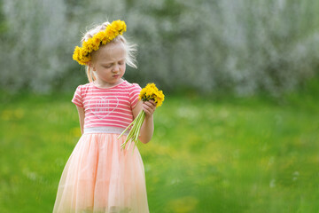 Sadness girl in green field with yellow dandelions. Little lady in pink dress holds flowers. Selective focus.