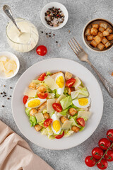 Caesar salad with lettuce, grilled chicken breast, boiled eggs, tomatoes, parmesan cheese and croutons in a ceramic plate on a concrete background. Top view.