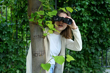 Close-up of a young woman watching someone with binoculars while hiding