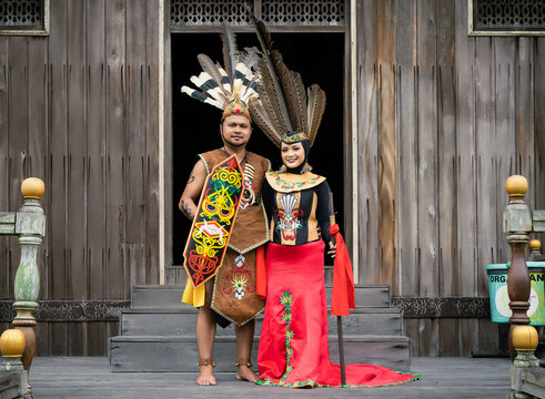 Portrait of man and woman wearing traditional Kalimantan Dayak clothing with the background of a traditional Dayat house called "Huma Betang"