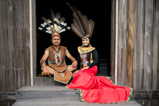Portrait of man and woman wearing traditional Kalimantan Dayak clothing with the background of a traditional Dayat house called "Huma Betang"
