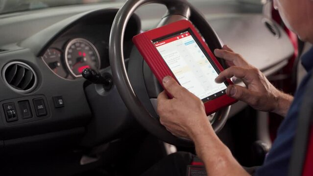 Auto electrician uses OBD2 scanner and tablet to diagnose vehicle faults. Professional mechanic checks car diagnostics, performs auto repair service, ensures vehicle maintenance, upgrades software.