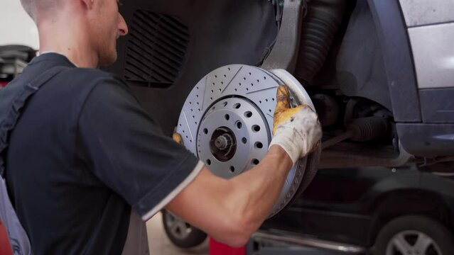 Auto mechanic installs new brake disc on vehicle. Car repair process in garage. Hands replace worn rotor with high-performance part. Brake system service, maintenance work shown step by step.