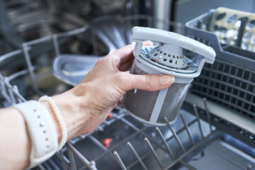 Close-up of a woman's hand putting a filter in the dishwasher.
