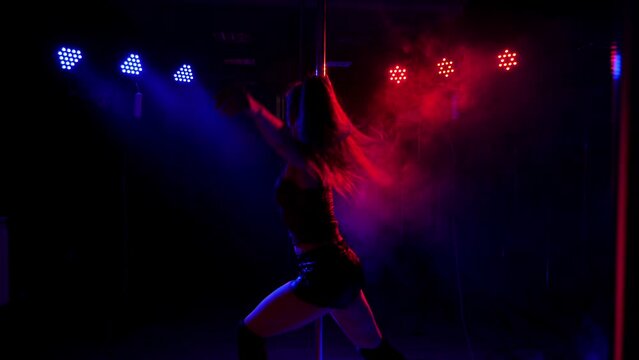 Young hot woman in sexy lingerie performs sensual pole dance, slow motion. Silhouette of a girl on the pole in a smoke-filled room.