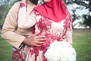 Malay bride and groom in elegant wedding outfits standing together during ceremony on sunny day.