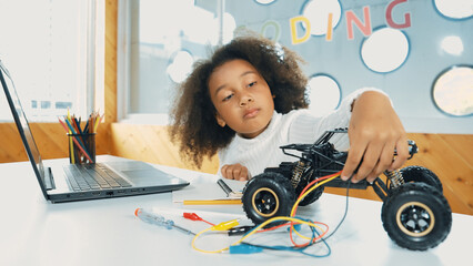 Smart african girl build robotic car while using wires while using laptop setting or writing prompt...