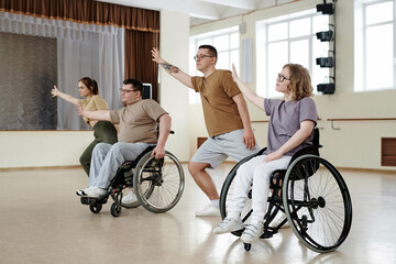 Fototapeta na wymiar Group of man and woman in wheelchairs and their partners practicing dance with wheelchairs in studio, long shot
