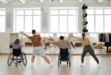 Rear view of four diverse men and women practicing dance with wheelchairs in front of mirrors in...