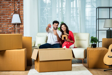 Indian couple holding piggy bank on home moving day  with cardboard boxes