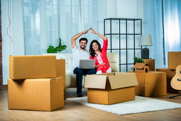Young Indian couple using laptop on sofa in midst of home shifting or home moving
