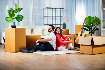 Home shifting or moving with indian young couple sitting on flore surrounded by cardboard boxes