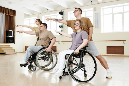 Group of four diverse Caucasian men and women practicing dance with wheelchairs in studio, long shot