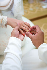 Groom put a ring on finger of his lovely wife. Close up image and selective focus.