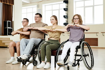 Group of four diverse men and women practicing dance with wheelchairs at class in studio, long shot