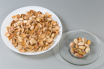 Partly peeling pistachio nuts on saucer against the empty shells