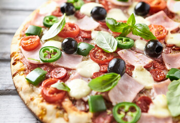 Pizza with ham, mozzarella cheese, cherry tomatoes, green and jalapeno pepper, black olives and fresh basil. Bright background. Close up.	