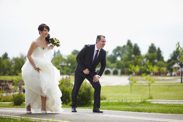The bride and groom are running along an asphalt road