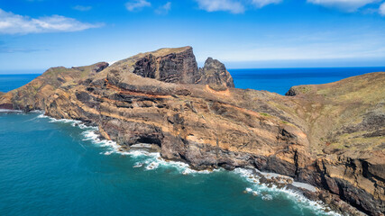 Fototapeta na wymiar The rocky coastline with a light blue sea, rocks, and green hills. It's a sunny day. PR8 trail in Madeira. It looks like a beautiful coastal landscape.