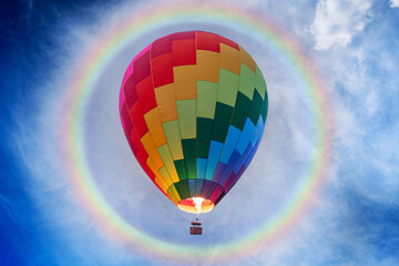 Colorful balloons soar in the sky with many flames and huge rainbow halo at noon.