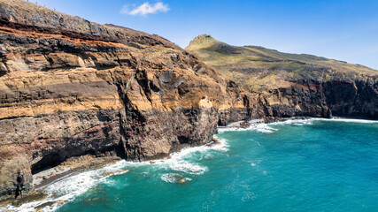 The rocky coastline with a light blue sea, rocks, and green hills. It's a sunny day. PR8 trail in...
