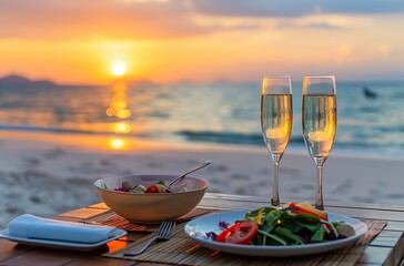 A table set with two plates of salad, one bowl and champagne glasses on the beach at sunset