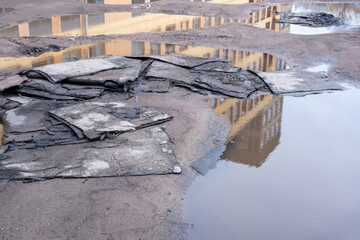 Sheets of old roofing felt lie in the puddles of a dirt road at a construction site