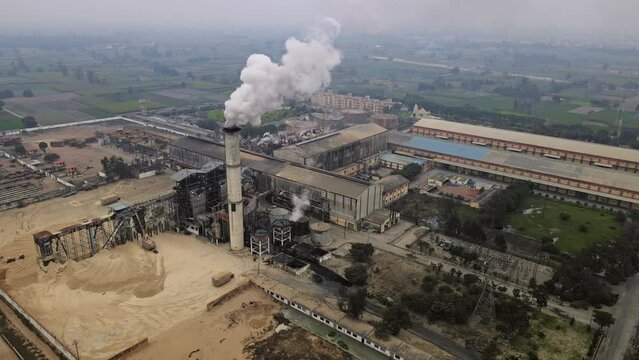 Aerial View: Industrial Area in India with Factories Emitting Smoke. Drone view of an Indian agro industry situated amidst large farming lands and forests.
