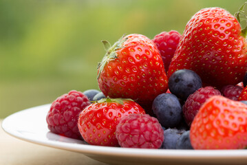 Pile od strawberries, blueberries, raspberries on white plate on green background