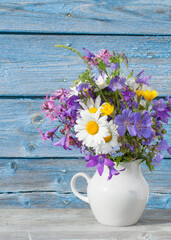 Bouquet of wildflowers in a white jug on a background of a blue wooden wall