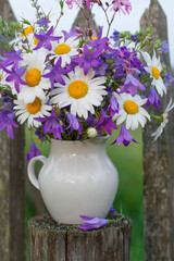 Bouquet of wildflowers in a white jug on an old wooden fence
