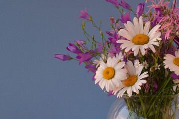 Bouquet of wildflowers in a round glass vase on a blue background

