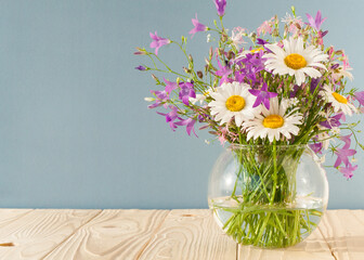 Bouquet of wildflowers in a round glass vase on a blue background

