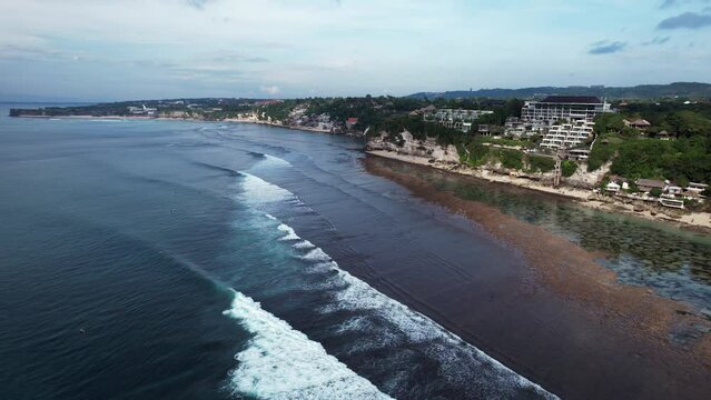 Aerial shot of mediocre waves at Padang Padang beach during low tide. Group of surfers stay on water, but waves not so good today. Wide angle shot from height, camera fly back