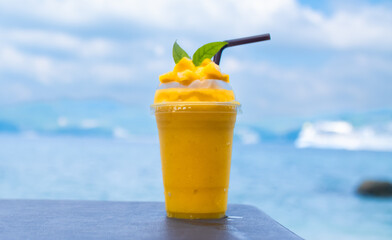 Smoothie made from fresh mango fruits against the backdrop of a seascape. Fruit and yoghurt ice cream decorated with leaves. Glass of tropical dessert close-up.