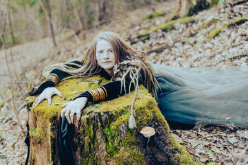 Female shaman in pristine forest nature laying on  tree stump, gold jewelry, shaggy hair