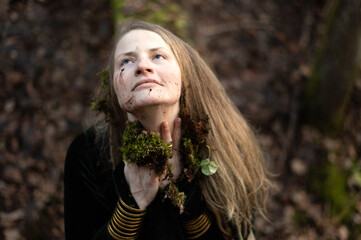Female shaman performs a nature ritual by smearing her face with forest moss and soil