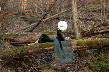 A woman lying on a tree trunk plays a shamanic drum on a spring day