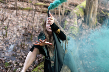 Shaman female holding hand green smoke bomb on  tree trunk in sping day