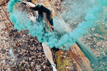 Shaman female holding hand green smoke bomb on  tree trunk in sping day