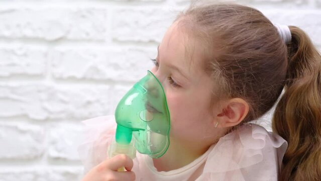 Little girl makes inhalation with medical nebulizer while sitting on bed. Cute child is sick bronchitis or asthma and breathes through inhaler at home