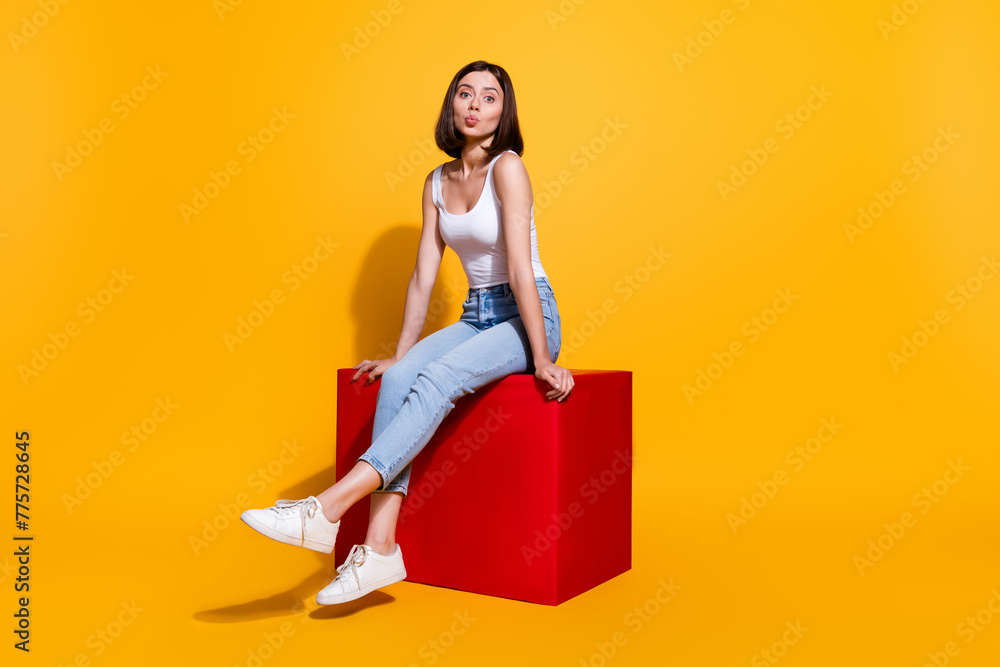 Sticker Full length photo of flirty sweet woman wear white singlet sitting red cube sending kiss isolated yellow color background