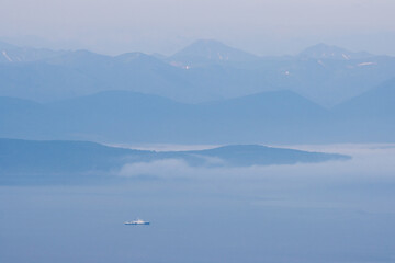 View of the coast guard ship in the bay. Mountains in the distance. Fog over the water. Morning seascape. Border region of Russia. Avacha Bay, Pacific Ocean. Kamchatka Peninsula, Russian Far East.