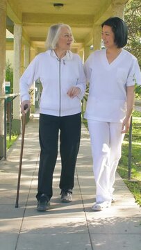 Asian doctor helps elderly woman while walking in the hospital garden. Vertical Video