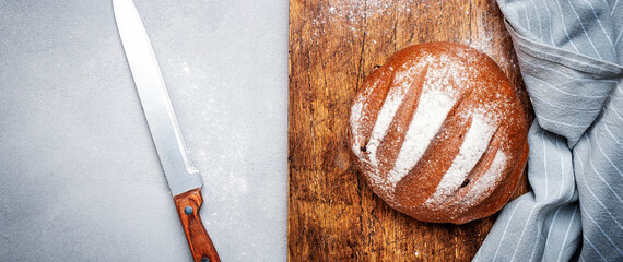 Sourdough rye bread on wooden board, bread knife and black kitchen towel. Gray table background,...