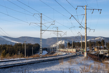 View of the railway turn. In the distance there is a village and mountains. Electrical pylons near the railway. Winter landscape. Baikal-Amur Mainline (BAM), East Siberian Railway. Siberia, Russia.